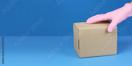hand in pink medical glove hold cardboard box on table, goods delivery in virus quarantine, copy space blue background