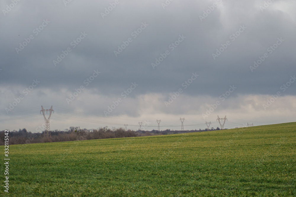 Green grass meadow, agricultural field, cloudy weather, electricity pylons in the back, natural background Green grass meadow, agricultural field, cloudy weather, electricity pylons in the back, natural background