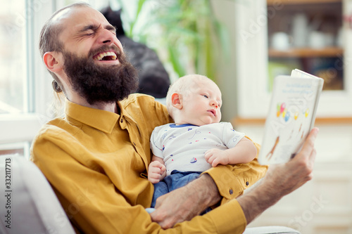 Father and his son on a armchair having fun and reading book. Young father reading book to his child baby infant. 