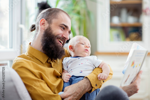 Father and his son on a armchair having fun and reading book. Young father reading book to his child baby infant. 