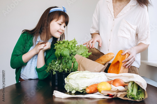 Unpacking an eco bag of fresh vegetables and greens after grocery shopping by two girls. Healthy eating concept.