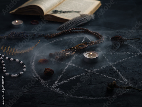Pentagram circle with a candle , an old book and amulets on the table . The concept of occultism , dark magic, divination or Halloween