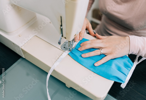 Woman hands using the sewing machine to sew the face home made diy medical mask during the coronavirus pandemia.