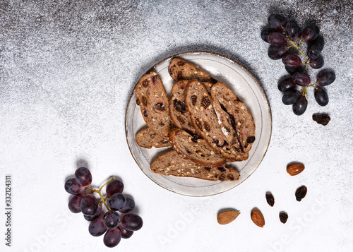 Sliced rusk fruit bread on a plate with red grapes, rosins and almond nuts. Homemade healthy food concept. View from above. Copy space. photo