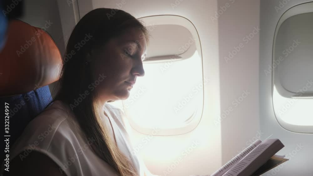 nice girl with brown hair wearing grey t-shirt reads book against bright porthole in liner passenger cabin closeup nice girl with brown hair wearing grey t-shirt reads book against bright porthole in liner passenger cabin closeup