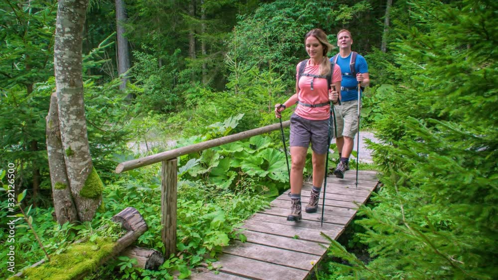 Woman and man hiking over small wooden bridge inside forest, approaching camera Woman and man hiking over small wooden bridge inside forest, approaching camera