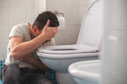 Man feeling bad putting his head in toillet and vomiting. photo