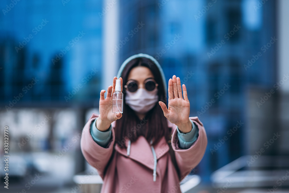 Fototapeta premium Close up hands of female in medical mask cleaning her hands with sanitizer outdoor in the city to prevent virus deseases. Coronavirus, COVID-19, epidemic, pandemic, quarantine concept.