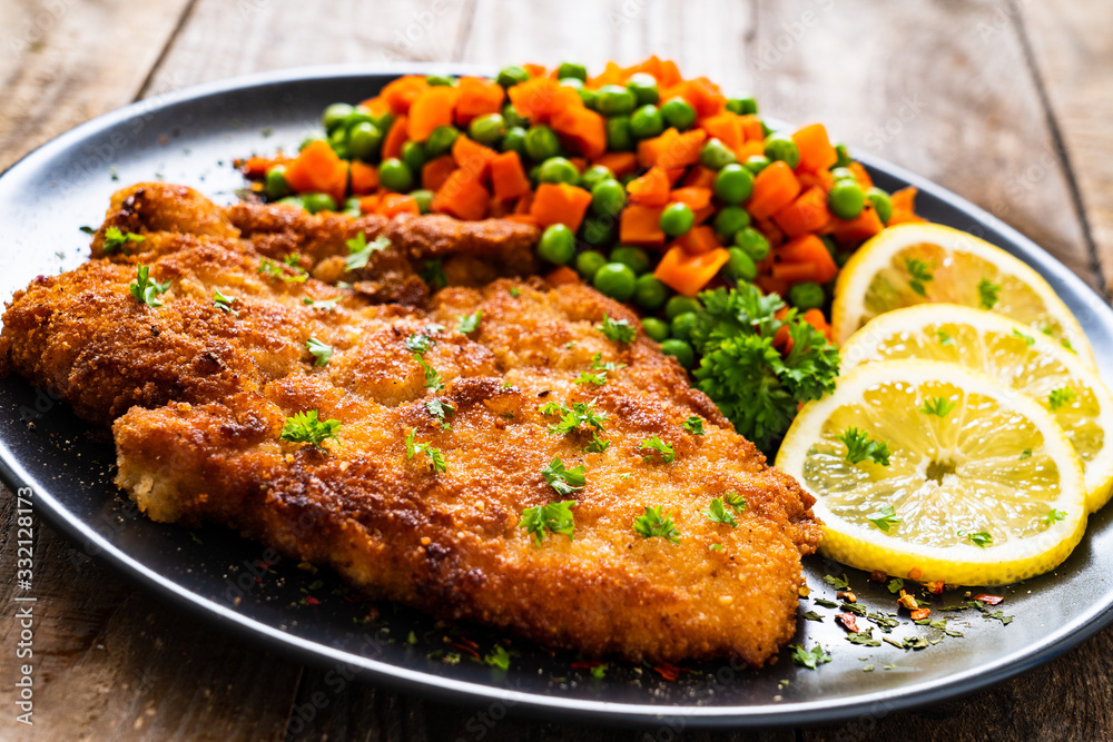 Schnitzel with boiled carrot and peas on wooden background