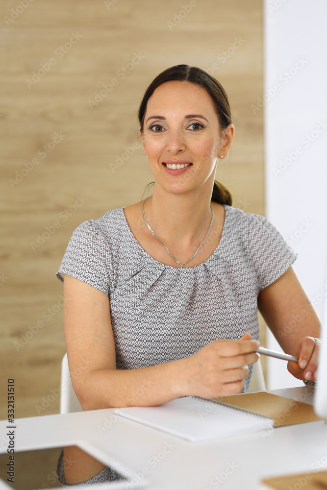 Cheerful smiling business woman working with pc computer while sitting at the desk in modern office. Middle aged female lawyer or auditor at work. Business people concept Cheerful smiling business woman working with pc computer while sitting at the desk in modern office. Middle aged female lawyer or auditor at work. Business people concept