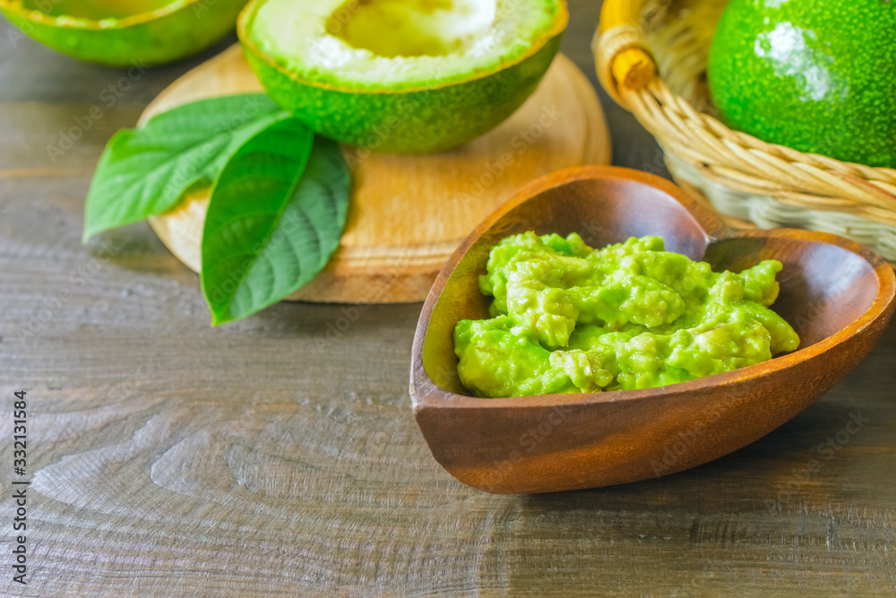 avocado puree and avocado halves close -up. avocado puree in a wooden bowl close- up on the table and green ripe avocados. avocado puree and avocado halves close -up. avocado puree in a wooden bowl close- up on the table and green ripe avocados.
