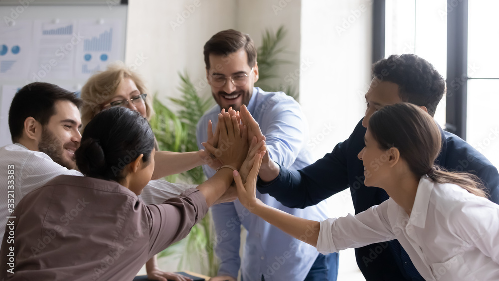 Overjoyed multiracial businesspeople give high five celebrate shared business victory or win, excited multiethnic colleagues engaged in teambuilding activity at meeting or briefing in office - obrazy, fototapety, plakaty 