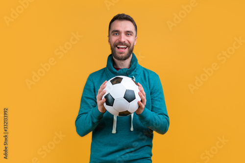 Young bearded casually dressed fan smiling and posing with soccer ball in hand on bright colored yellow background © wpadington