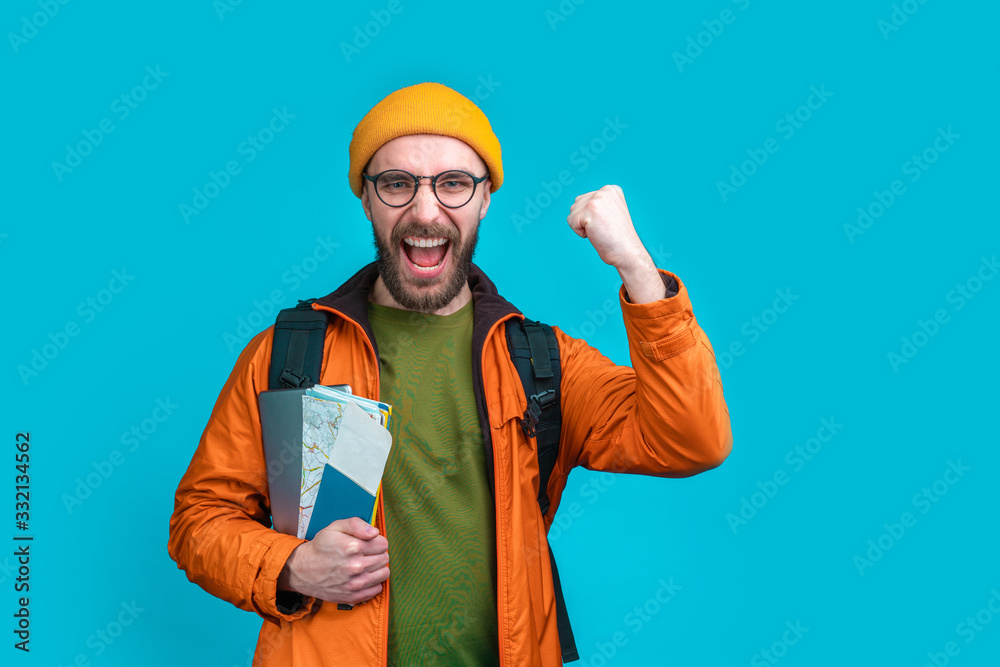 Half length studio portrait of casually dressed smiling male tourist with a backpack isolated over blue background