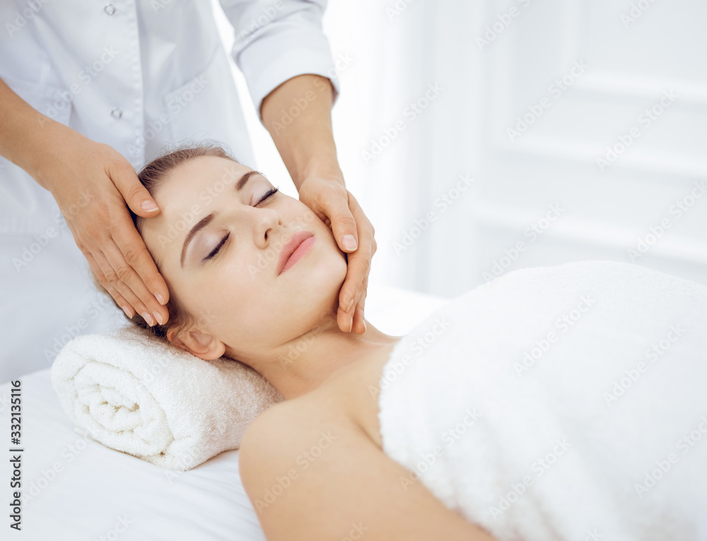 Young and blonde woman enjoying facial massage in spa salon. Beauty concept Young and blonde woman enjoying facial massage in spa salon. Beauty concept