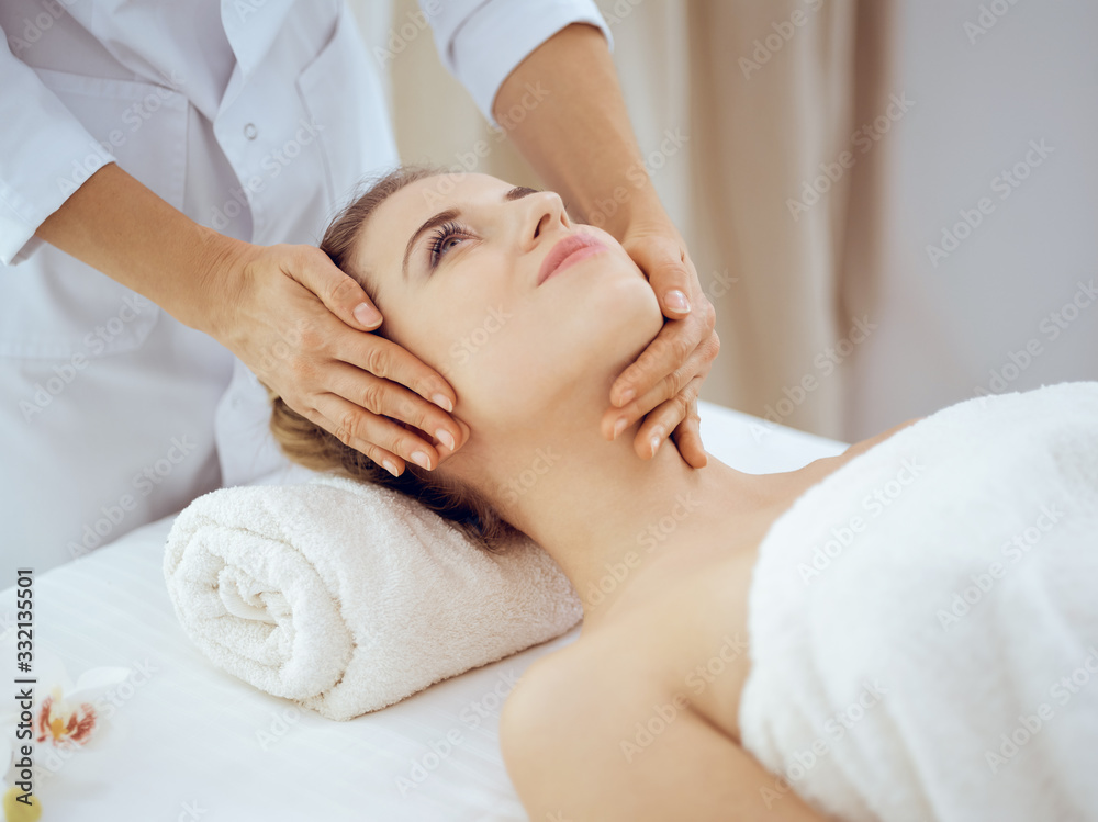 Young and blonde woman enjoying facial massage in spa salon. Beauty concept Young and blonde woman enjoying facial massage in spa salon. Beauty concept