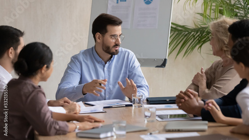 Concentrated businesspeople gather at desk in boardroom brainstorm consider ideas together, focused diverse multiracial colleagues talk discuss business project or paperwork at meeting in office
