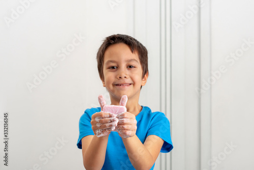Smiling little boy wearing a blue shirt washing hands with pink soap.