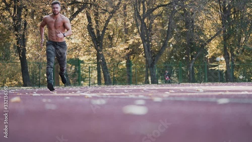 Healthy athlete is running in the stadium. Young sportsman is involved in sport running on the autumn trees background. View from below. photo