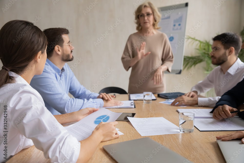 Serious businesspeople sit at desk in boardroom brainstorm discuss paperwork statistics together, concentrated colleagues gather at office briefing consider business project, cooperation concept