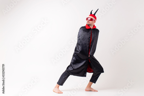 Stylish elegant man in black red halooween costume and devil horns posing like an eccentric actor over white studio background.