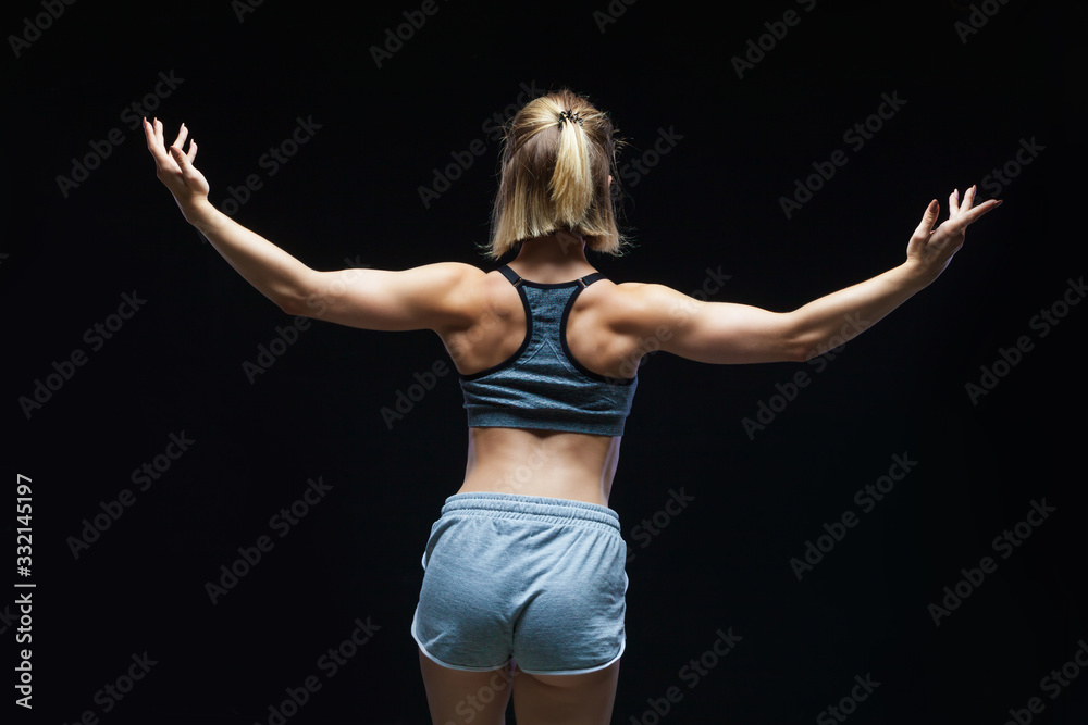 Back view of strong sporty girl in top and jean shorts showing muscles on black background Back view of strong sporty girl in top and jean shorts showing muscles on black background