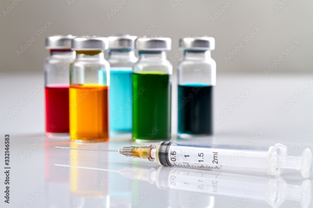 Syrynge and bottles with colored medicine. White clean reflective surface. Syrynge and bottles with colored medicine. White clean reflective surface.