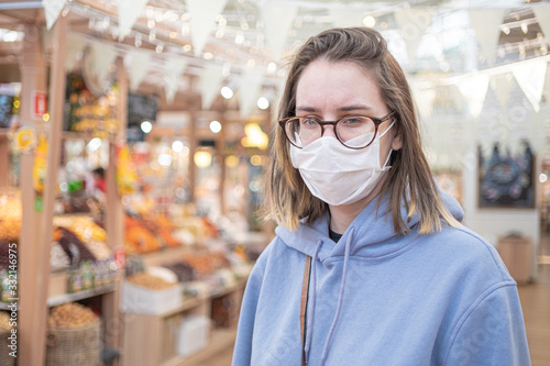 Woman in medical face mask walking in modern grocery market, shop. Corona virus protection, quarantine, self distancing
