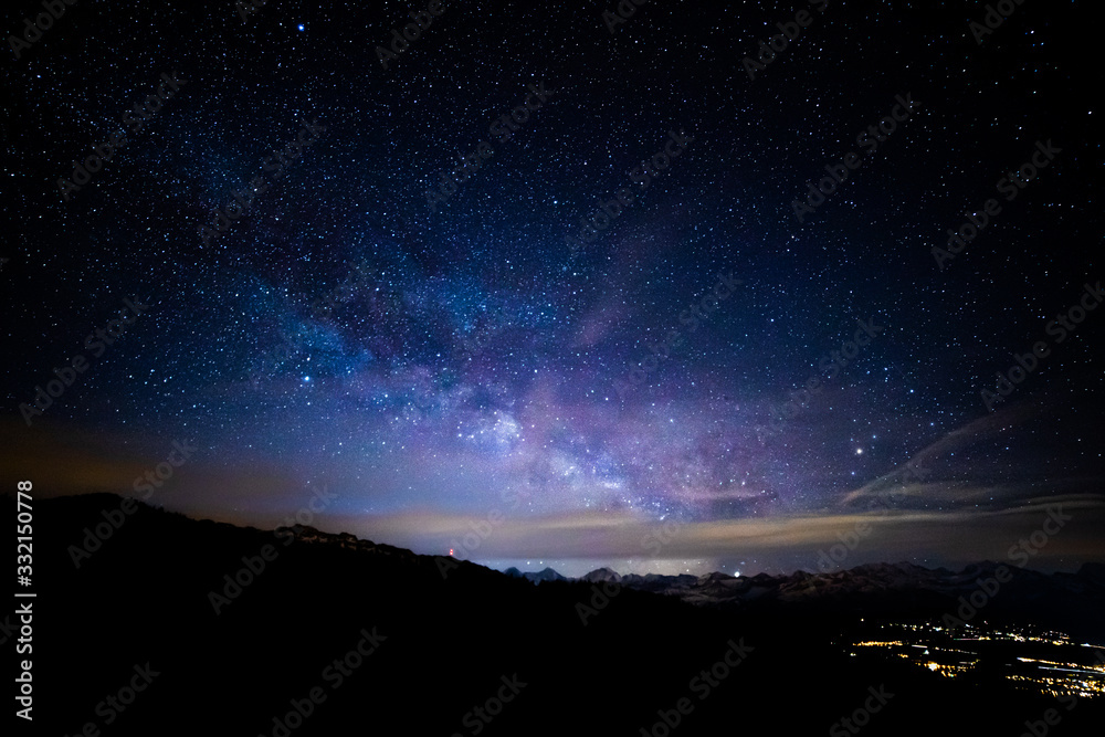 The Milky Way above the city and the mountaints with a cloudy stripe at the horizon