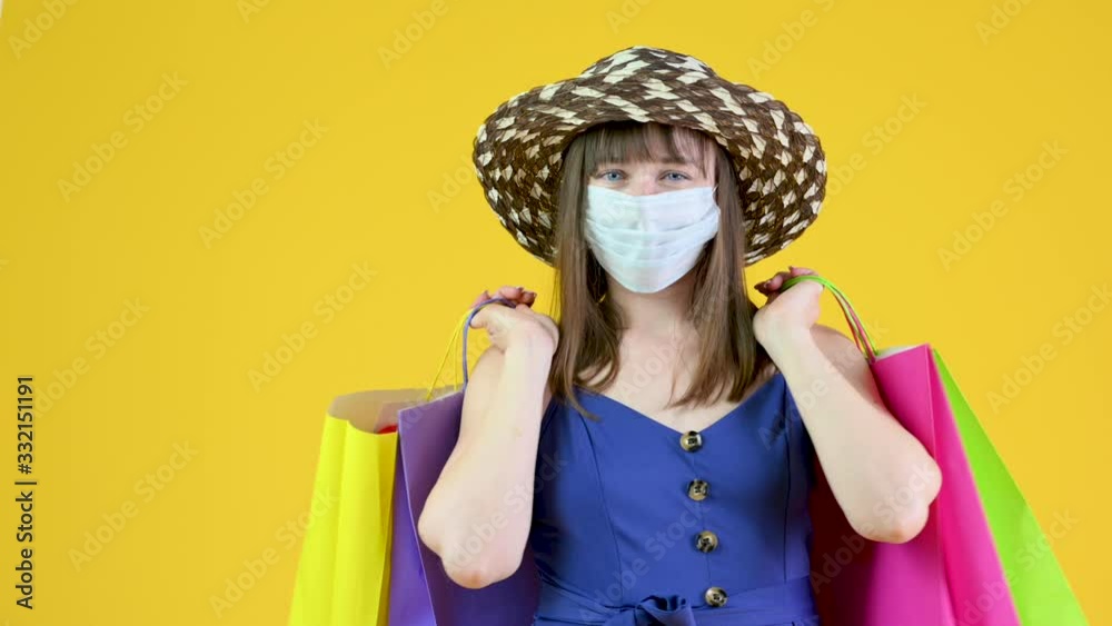 A young girl in a medical mask is clutching shopping bags in her hands. Isolated on a yellow background. ealth care and medical concept.