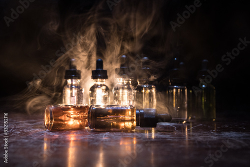 Smoke clouds and vape liquid bottles on dark background. Light effects. Useful as background or vape advertisement or vape background. Selective focus