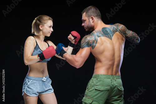 Young muscular woman and man in boxing gloves practicing isolated on black © satyrenko