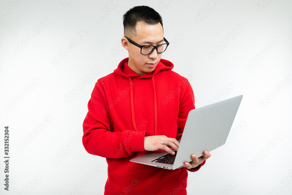 attractive brunette man in casual red hoodie with a laptop in his hands on a white studio background attractive brunette man in casual red hoodie with a laptop in his hands on a white studio background