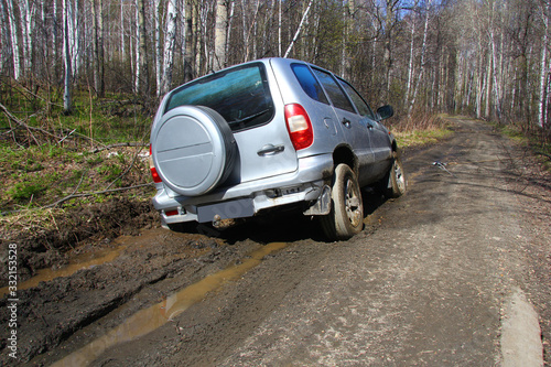 a grey SUV is towed by a hand winch out of the mud on a forest road © Дядя Фёдор