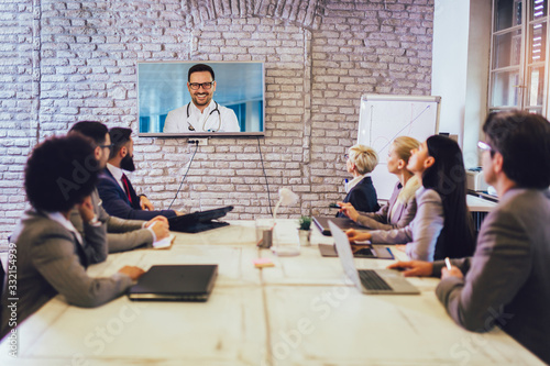 Team of business people looking doctor speech at projector screen in video conference