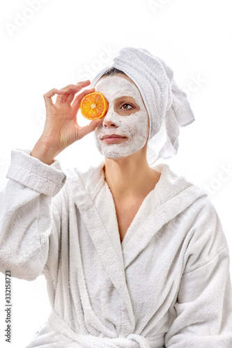 Beautiful woman with a white cosmetic mask on her face and slices of oranges in her hand.