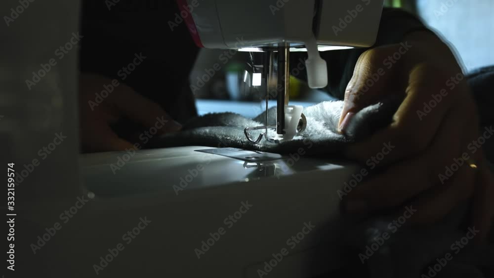Needle for sewing machine in motion. The close-up of the sewing machine needle quickly moves up and down. The seamstress sews gray fabric in the sewing workshop. The process of sewing the fabric. Needle for sewing machine in motion. The close-up of the sewing machine needle quickly moves up and down. The seamstress sews gray fabric in the sewing workshop. The process of sewing the fabric.
