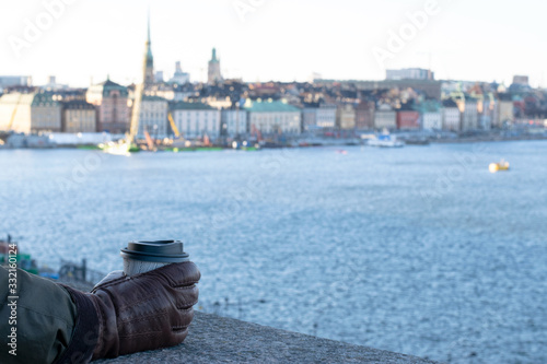 Photography Hand with gloves holding a take away coffee mug with the city skyline and water in the background