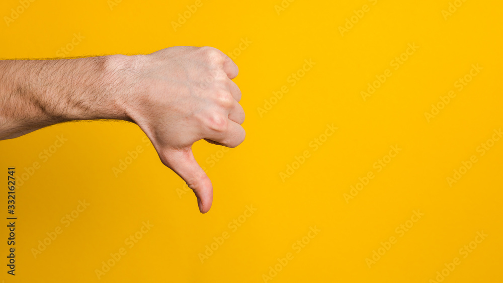 not good and not approved. close up hand of a man showing thumb down dislike sign over yellow background with copyspace for design