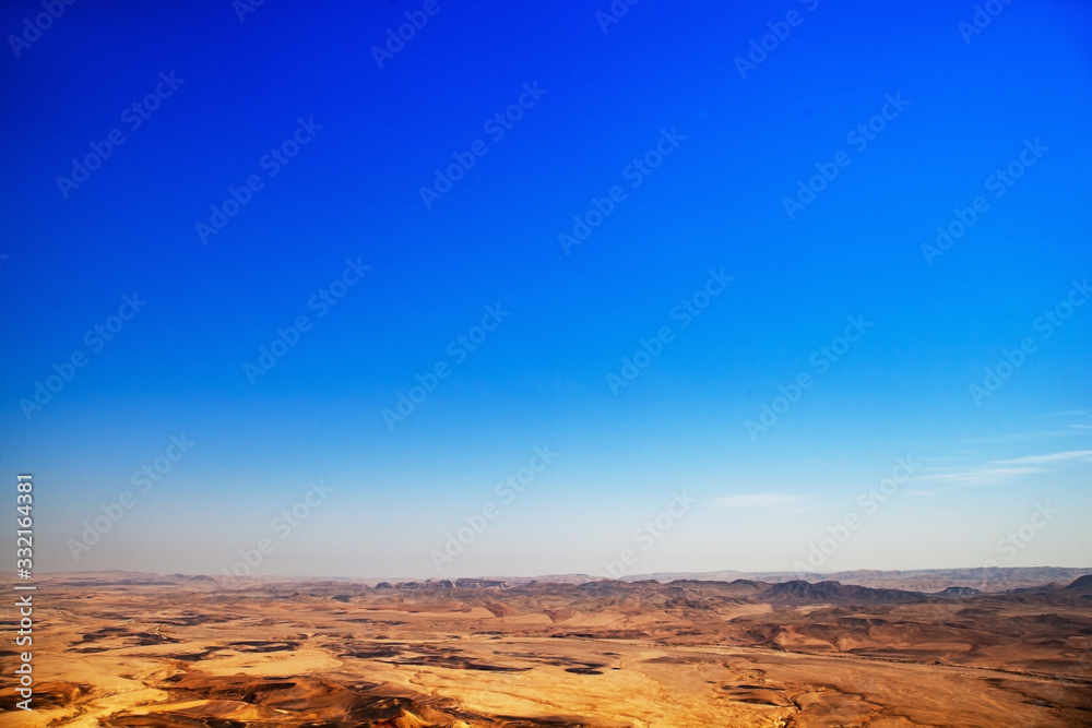 The desert during the day and above it is a huge blue sky. The scorched earth which has no punishment, a hot daylight in the desert. No animal trees and shade.