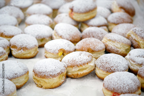 Round donuts sprinkled with white icing sugar with fruit jam. Homemade stuffed donuts on a parchment covered table. Sweet baking department in the store.