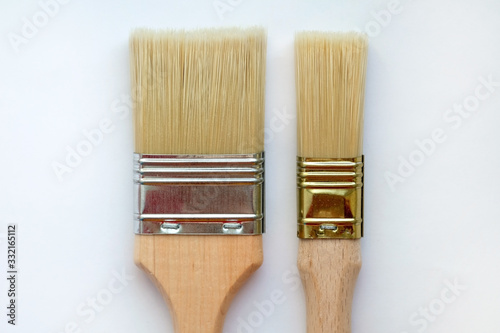 Fototapeta Naklejka Na Ścianę i Meble -  A wide paint brush and a small one on a white background top view. Paint brushes of different lengths and thicknesses. Two flat tassels with wooden handles.