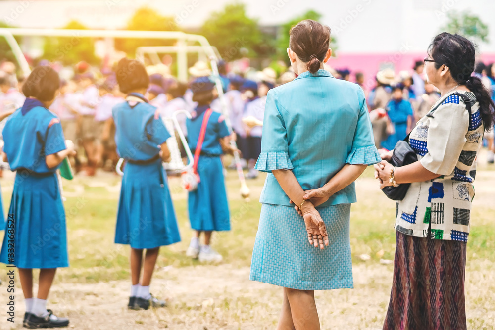 Asian female teacher stand to control the students playing music while lining up to pay respect to the national flag in the morning in school. Asian female teacher stand to control the students playing music while lining up to pay respect to the national flag in the morning in school.