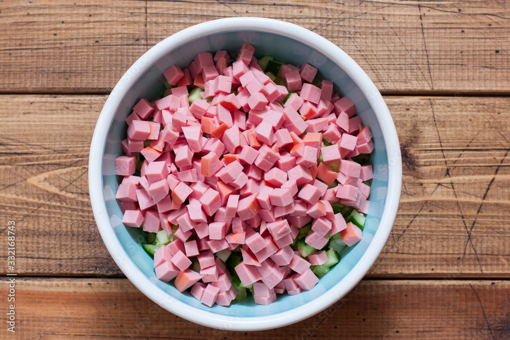 Step by step preparation of cold okroshka soup with sausage, step 4 - adding sliced sausage, top view, selective focus