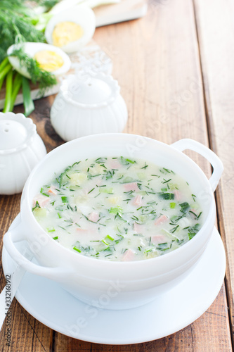 Traditional summer okroshka soup with sausage and vegetables in a white bowl, copy space