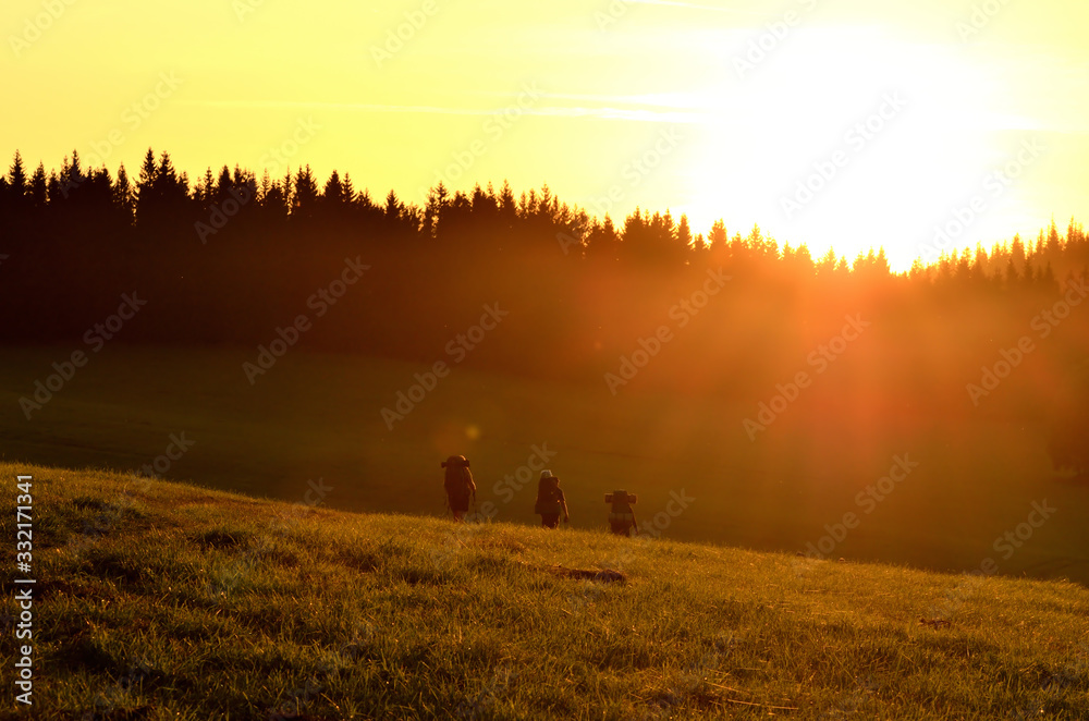 Hikers walking across the meadow towards the mountains by the sunset glow.