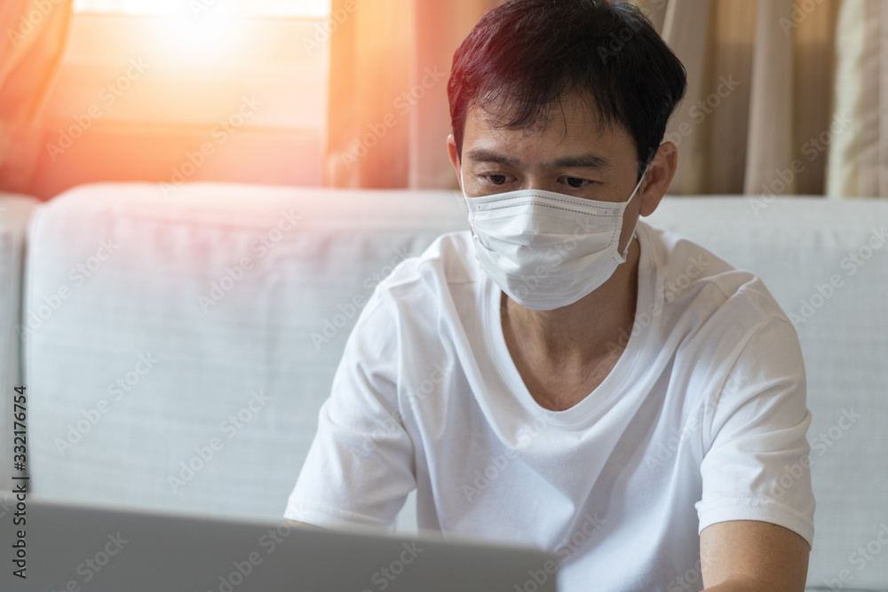 Work from home COVID-19 concept. Asia man wear medical mask using notebook computer working for social distancing meeting online with social media application Work from home COVID-19 concept. Asia man wear medical mask using notebook computer working for social distancing meeting online with social media application