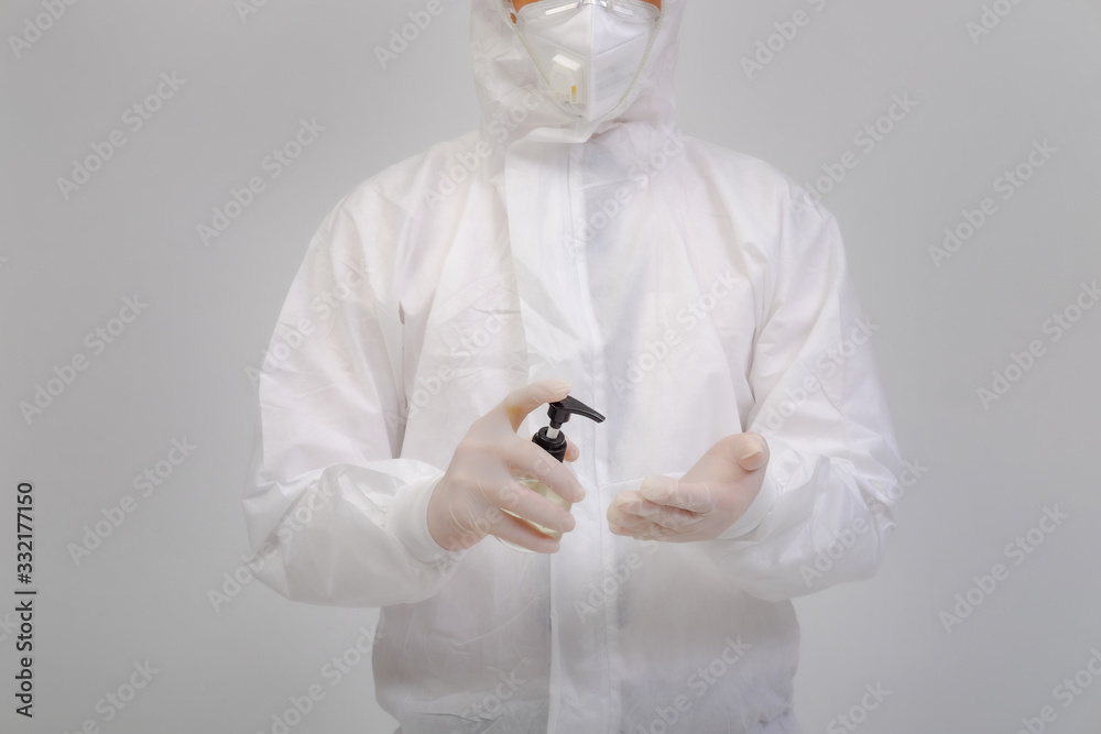 Male doctor wears protective suit, medical gloves and medical masks holding alcohol gel on gray background, corona virus concept, covid19 concept, medical concept Male doctor wears protective suit, medical gloves and medical masks holding alcohol gel on gray background, corona virus concept, covid19 concept, medical concept