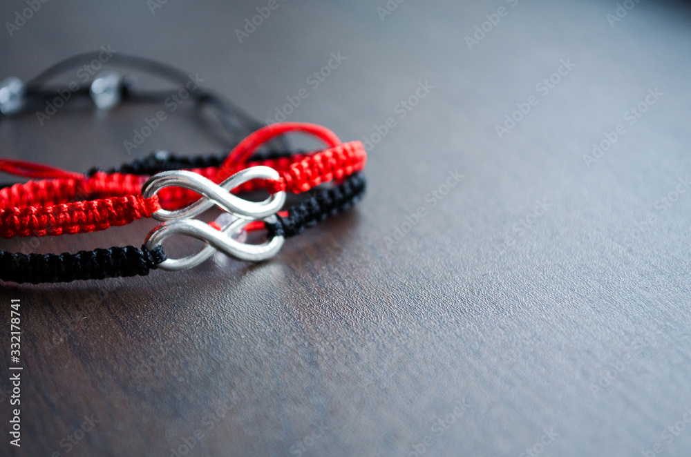 Pair bracelets for lovers with infinity. Red and black bracelets made of cord on a wooden background. Macro shot of handmade jewelry. Relationships and love. Girl and boy. Empty space in the photo. Pair bracelets for lovers with infinity. Red and black bracelets made of cord on a wooden background. Macro shot of handmade jewelry. Relationships and love. Girl and boy. Empty space in the photo.