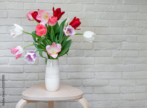bright tulips bouquet in a vase on a wooden table. white texture background. Greeting card with flowers, copy space. horizontal image.